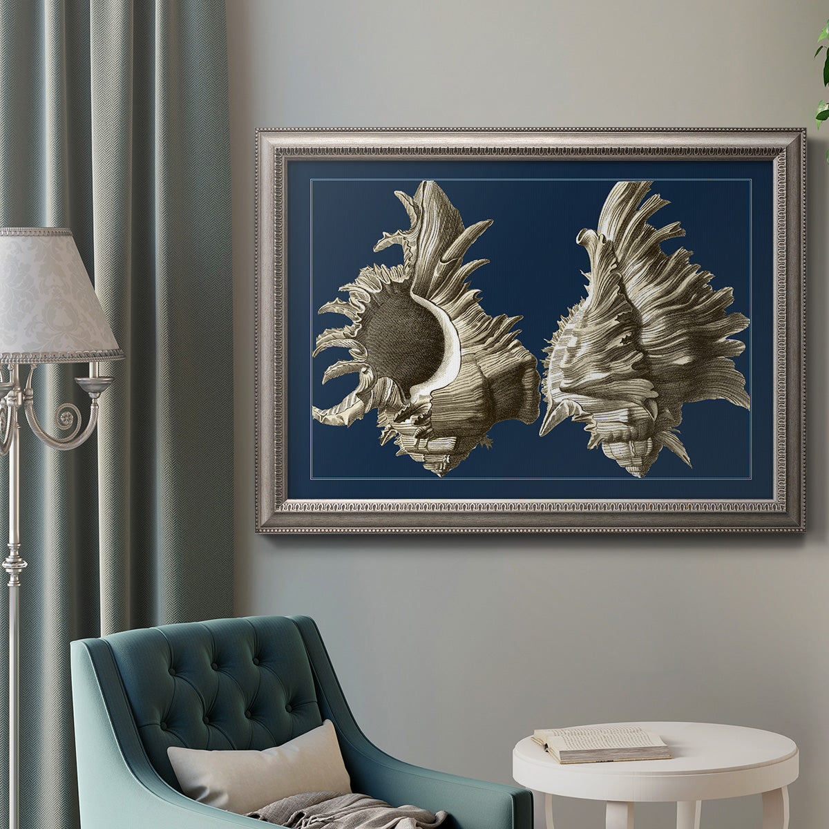 Vintage nautical conch shell artwork on navy background in an ornate vintage silver frame displayed in a neutral interior setting.