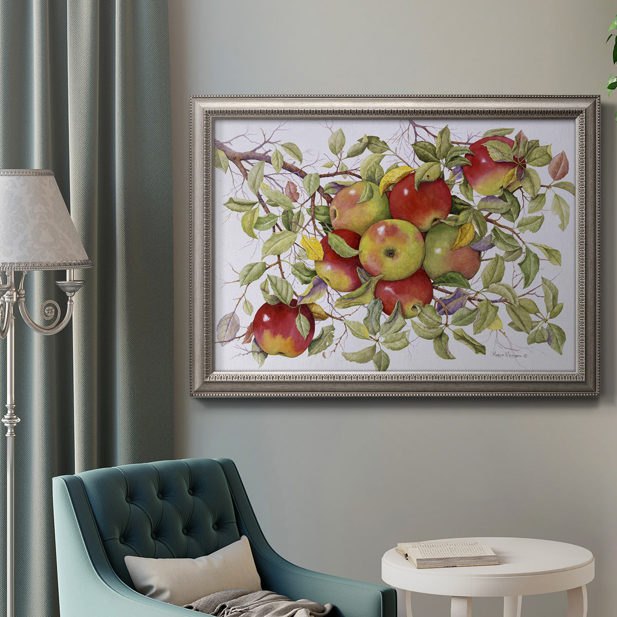 Classic still life painting of apples in an ornate vintage silver frame displayed in a neutral interior setting.