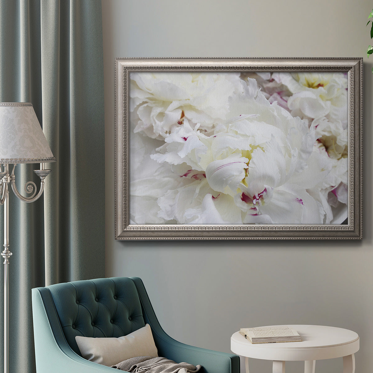 White peonies in bloom in an ornate vintage silver frame displayed in a neutral interior setting.