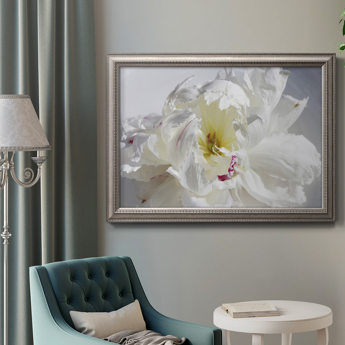 Soft white peony close-up in an ornate vintage silver frame displayed in a neutral interior setting.