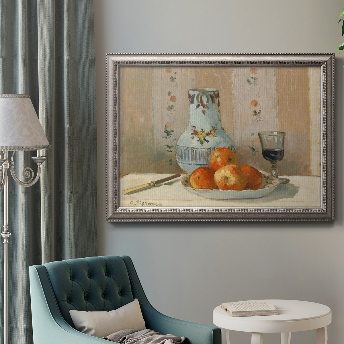 Impressionist still life painting with apples and a ceramic pitcher in an ornate vintage silver frame displayed in a neutral interior setting.