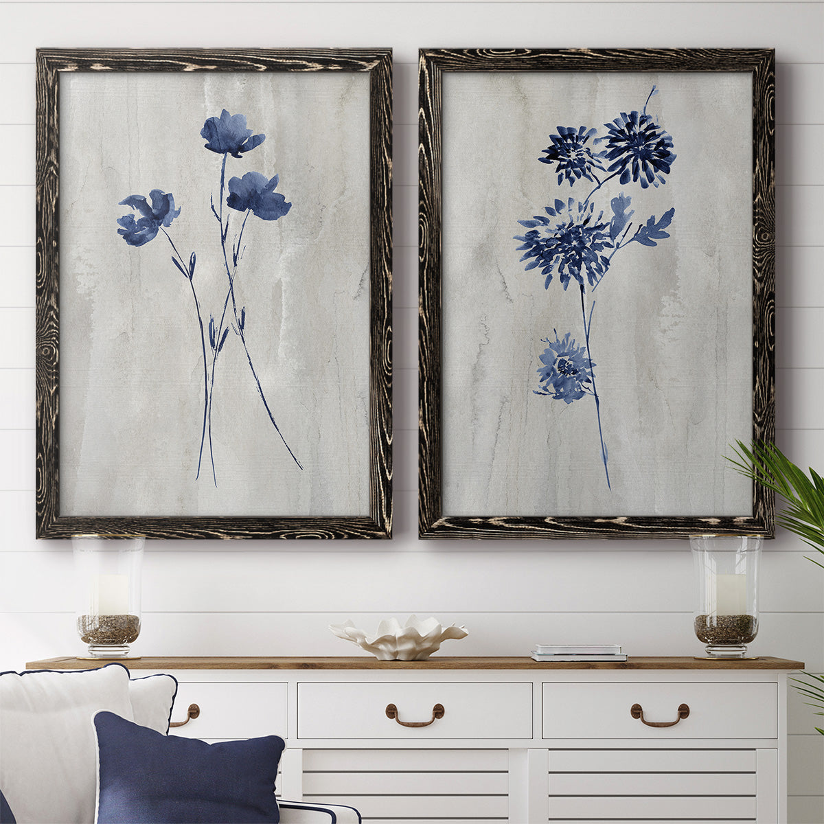 Set of two black barnwood framed canvas prints depicting a coordinated art pair of blue wildflower stems on weathered neutral paper rendered as rustic monochrome botanical paintings above a dining room sideboard.