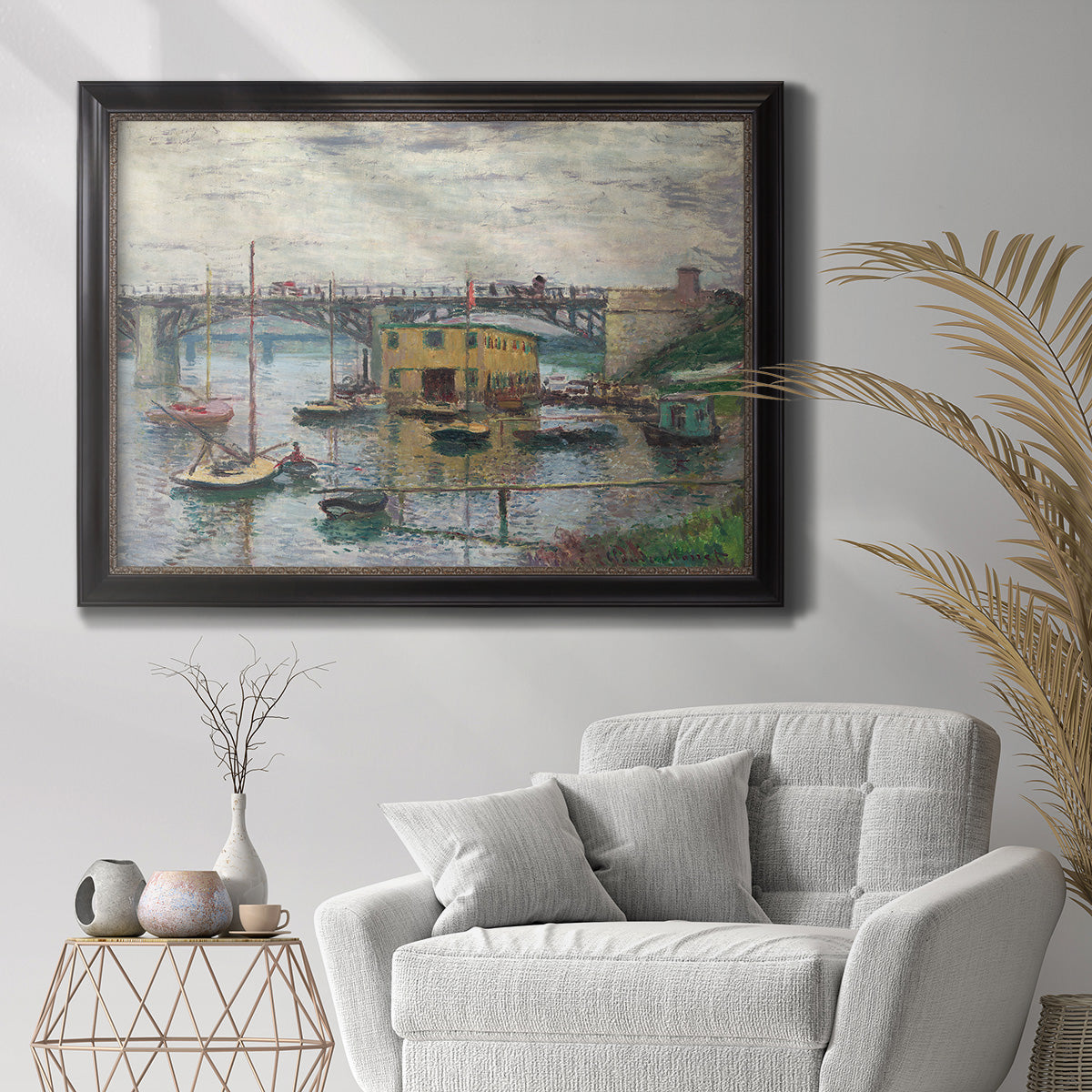 Impressionist river bridge scene on an overcast day by Claude Monet in an ornate black frame with gilded inner detail displayed in a bright interior setting.