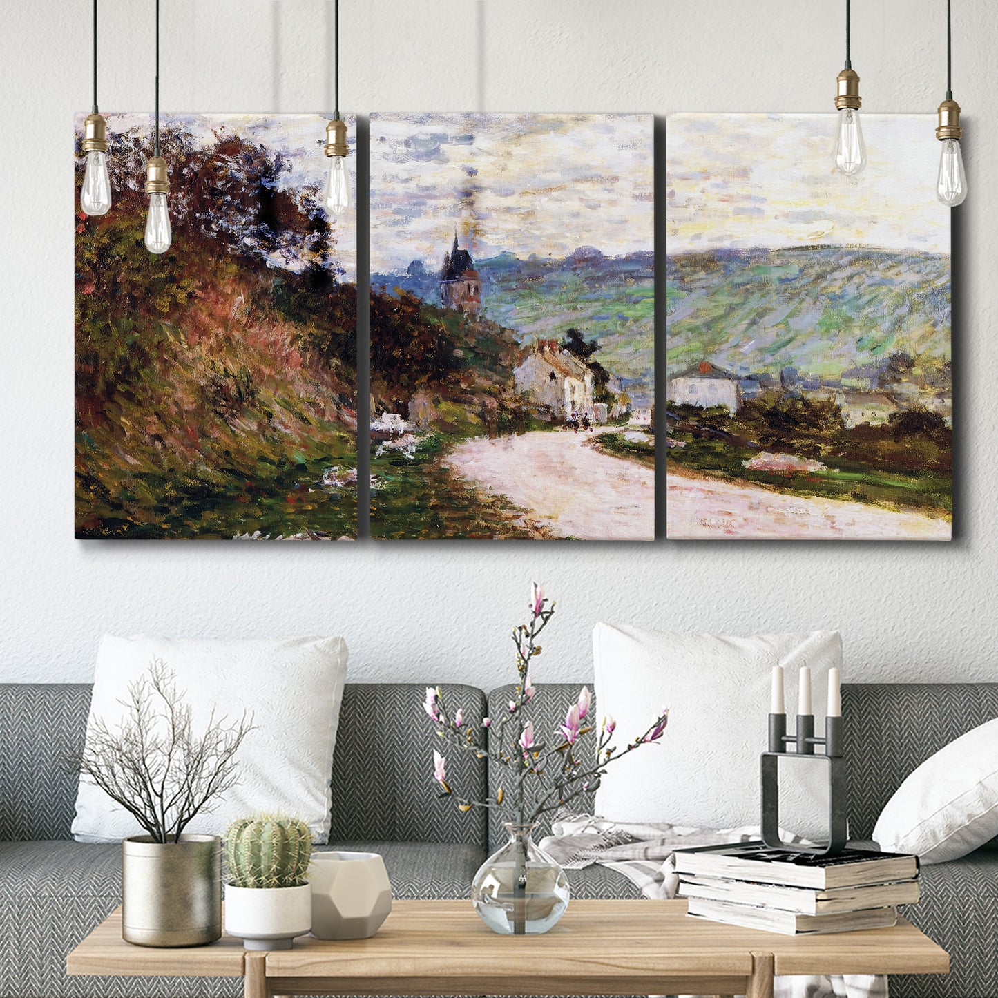 Three-panel canvas wall art featuring country road through village, displayed in a modern living room above seating.
