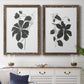 Set of two walnut barnwood framed canvas prints depicting a coordinated art pair of black leafy vine silhouettes rendered as minimalist botanical prints above a dining room sideboard.