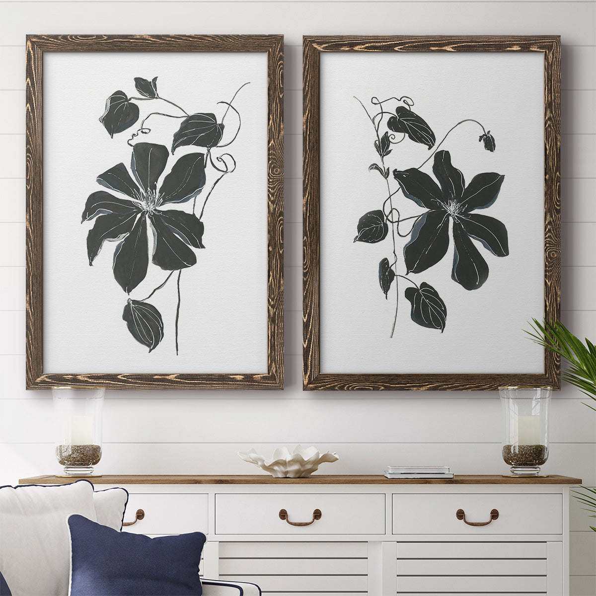 Set of two walnut barnwood framed canvas prints depicting a coordinated art pair of black leafy vine silhouettes rendered as minimalist botanical prints above a dining room sideboard.