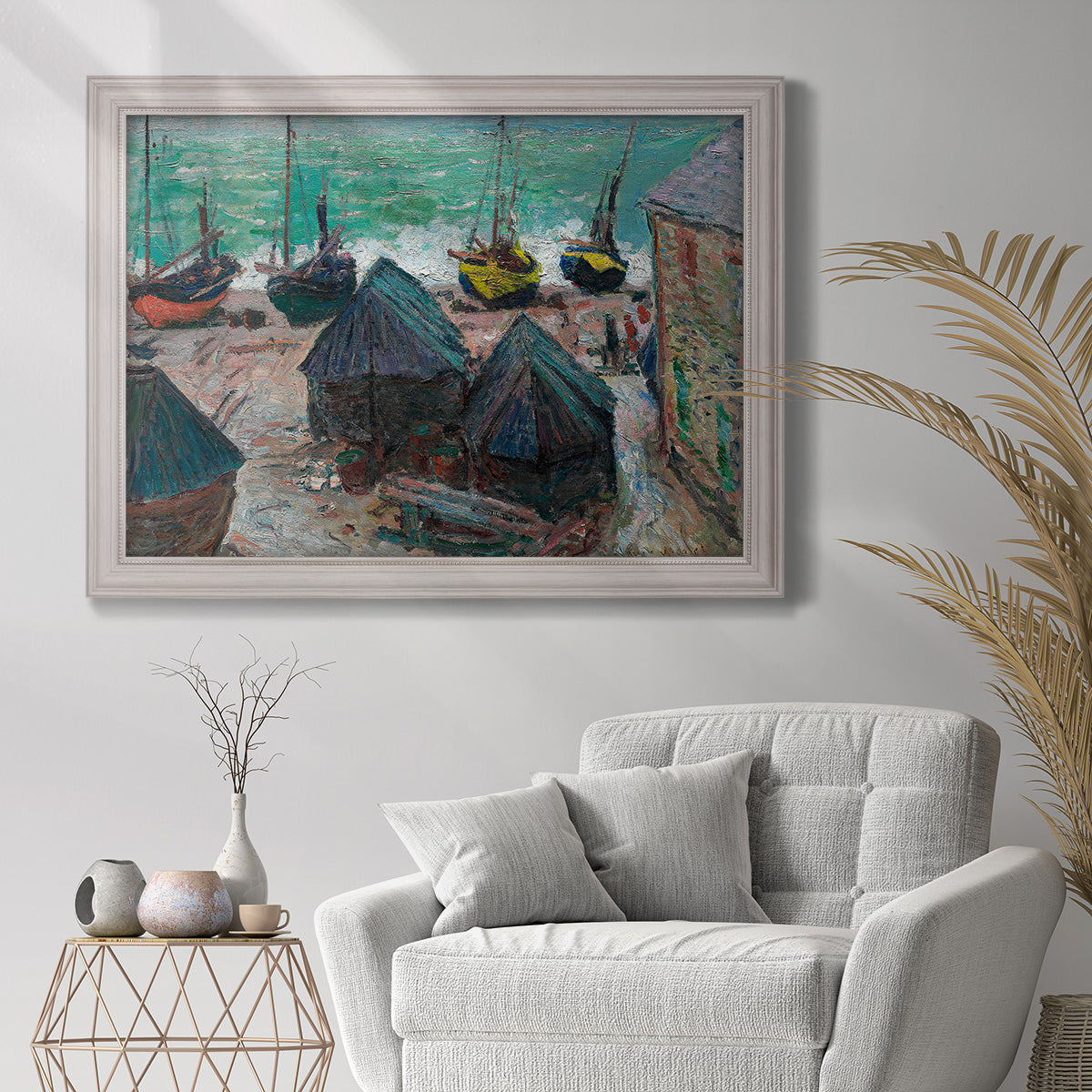 Impressionist coastal beach scene with boats by Claude Monet in an ornate weathered white frame displayed in a bright interior setting.