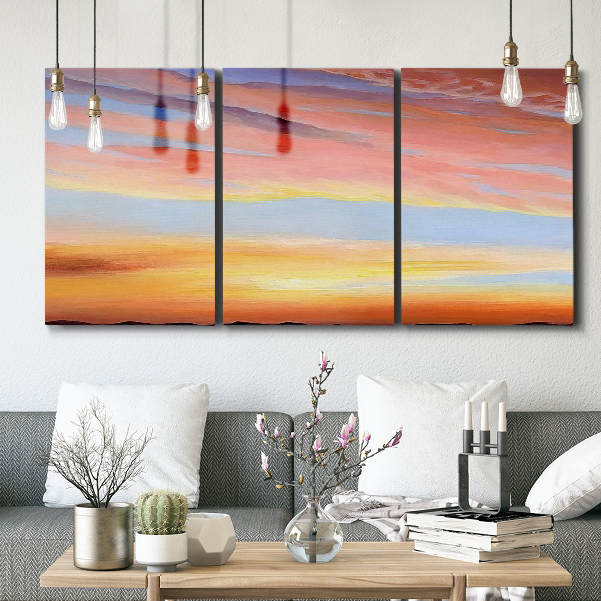 Three-panel canvas wall art featuring glowing sunset sky over landscape, displayed in a modern living room above seating.