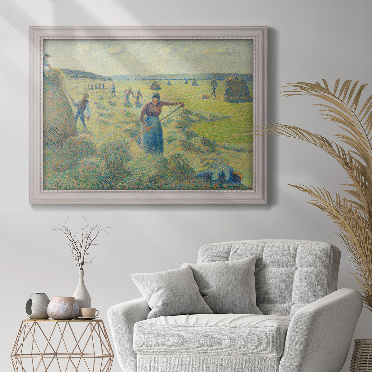 Impressionist rural hay harvest landscape by Camille Pissarro in an ornate weathered white frame displayed in a bright interior setting.