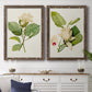 Set of two walnut barnwood framed canvas prints depicting a coordinated art pair of white magnolia blossoms and glossy green leaves rendered as traditional botanical paintings above a dining room sideboard.