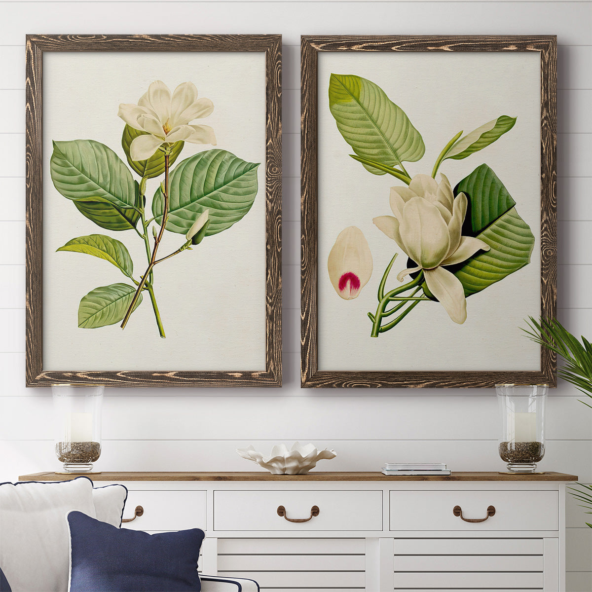 Set of two walnut barnwood framed canvas prints depicting a coordinated art pair of white magnolia blossoms and glossy green leaves rendered as traditional botanical paintings above a dining room sideboard.