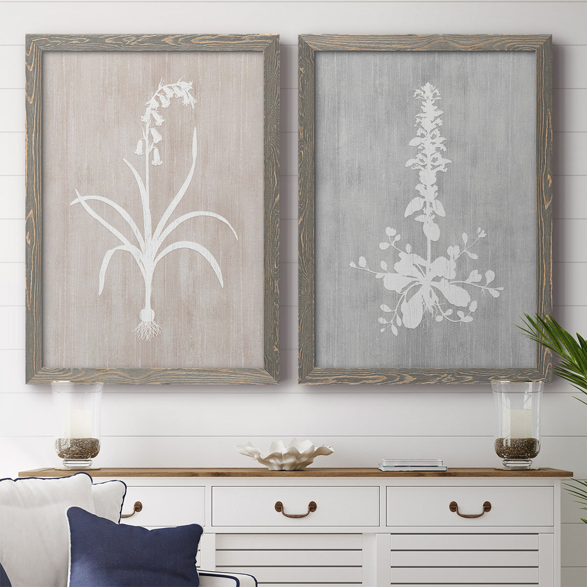 Set of two gray barnwood framed canvas prints depicting a coordinated art pair of white botanical silhouettes on softly weathered neutral backgrounds rendered as rustic minimalist botanical prints above a dining room sideboard.