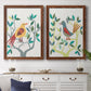 Set of two maple barnwood framed canvas prints depicting a coordinated art pair of stylized colorful birds perched among leafy branches rendered as modern folk-art bird illustrations above a dining room sideboard.