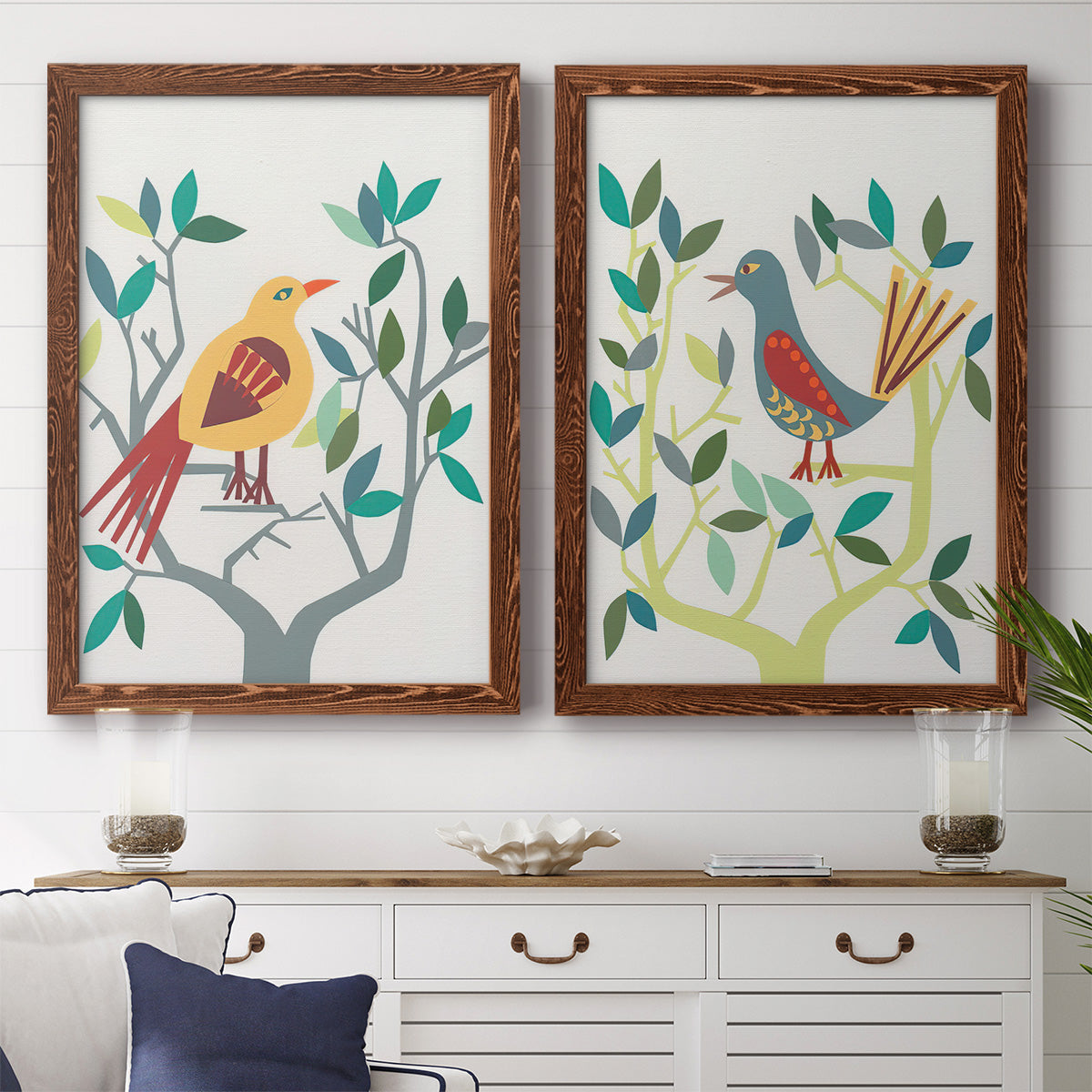 Set of two maple barnwood framed canvas prints depicting a coordinated art pair of stylized colorful birds perched among leafy branches rendered as modern folk-art bird illustrations above a dining room sideboard.