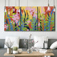 Three-panel canvas wall art featuring bold colorful floral abstraction, displayed in a modern living room above seating.