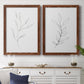 Set of two maple barnwood framed canvas prints depicting a coordinated art pair of single continuous-line leafy branches rendered as minimalist botanical line drawings above a dining room sideboard.