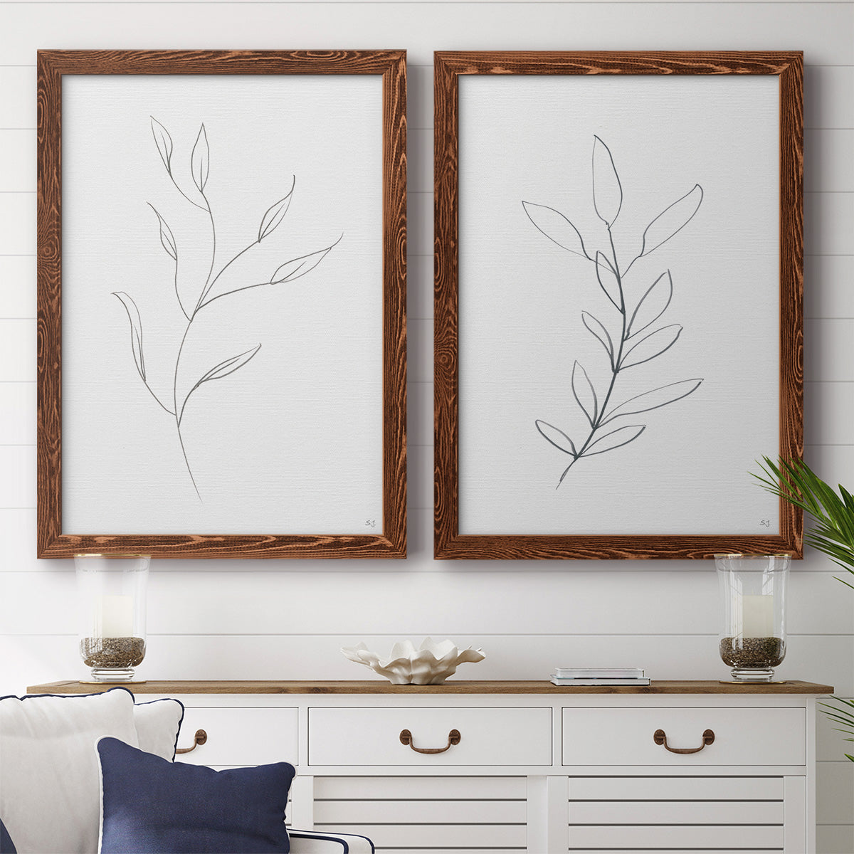 Set of two maple barnwood framed canvas prints depicting a coordinated art pair of single continuous-line leafy branches rendered as minimalist botanical line drawings above a dining room sideboard.