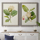 Set of two gray barnwood framed canvas prints depicting a coordinated art pair of white magnolia blossoms and glossy green leaves rendered as traditional botanical paintings above a dining room sideboard.