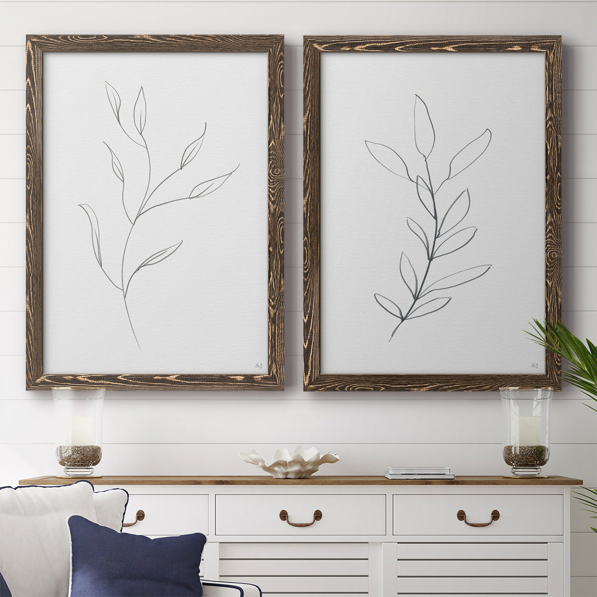 Set of two walnut barnwood framed canvas prints depicting a coordinated art pair of single continuous-line leafy branches rendered as minimalist botanical line drawings above a dining room sideboard.