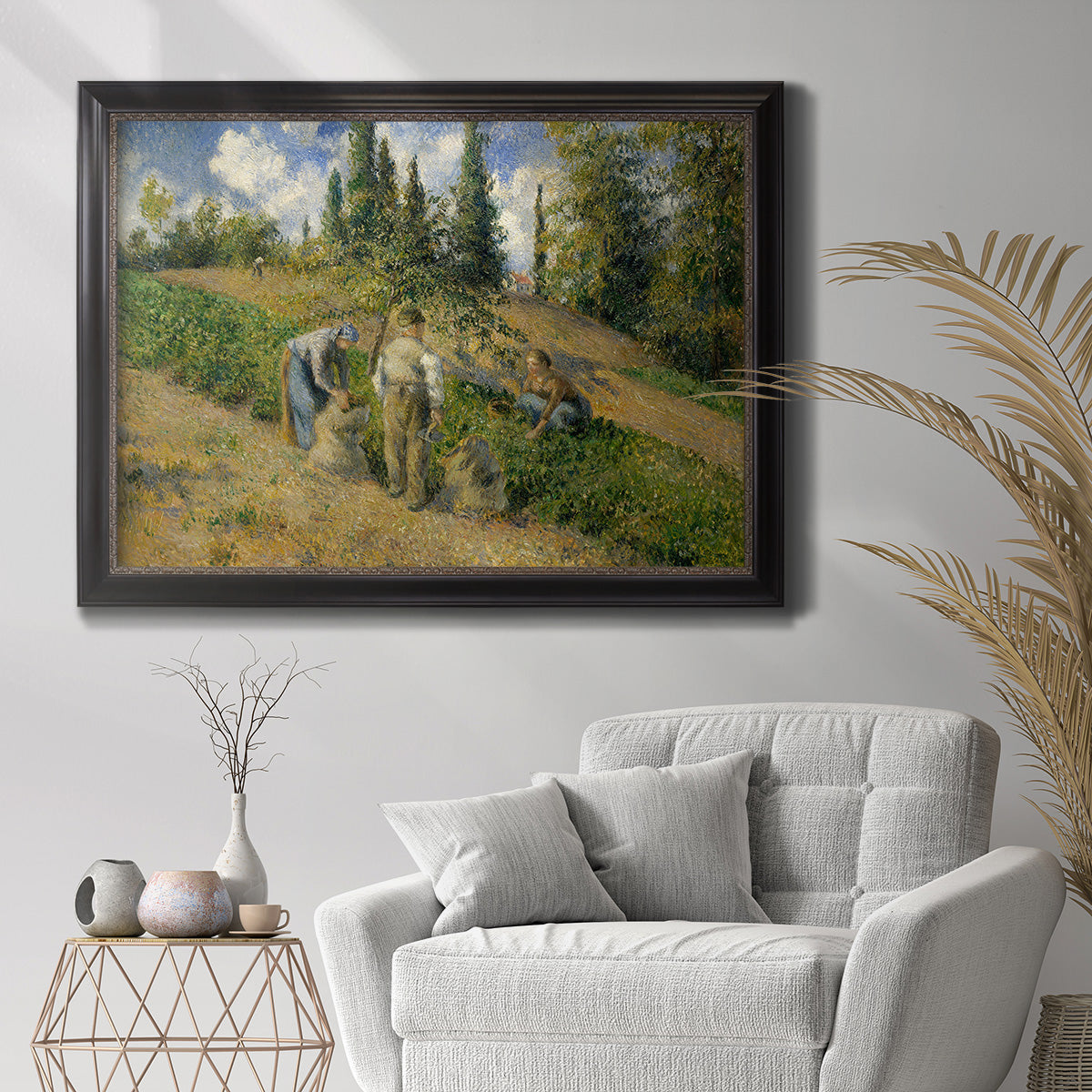 Impressionist countryside harvest scene by Camille Pissarro in an ornate black frame with gilded inner detail displayed in a bright interior setting.