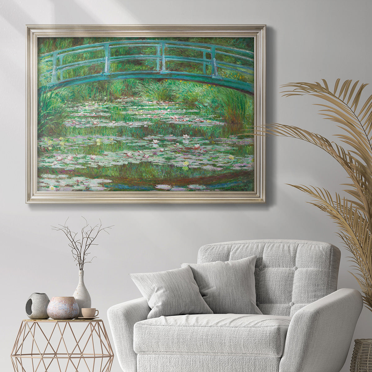 Impressionist garden scene with Japanese bridge and water lilies by Claude Monet in an ornate champagne frame displayed in a bright interior setting.