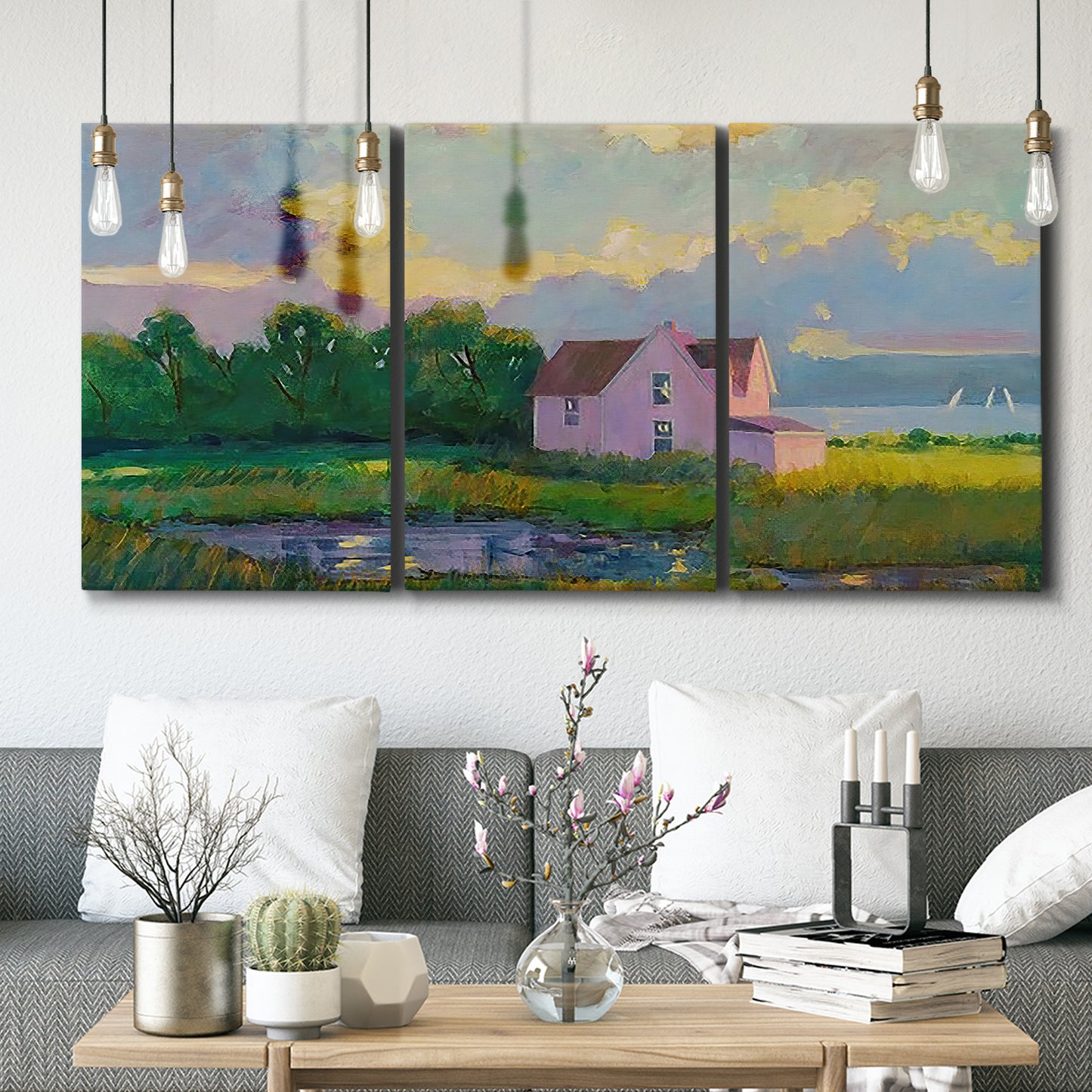 Three-panel canvas wall art featuring farmhouse near coastline landscape, displayed in a modern living room above seating.