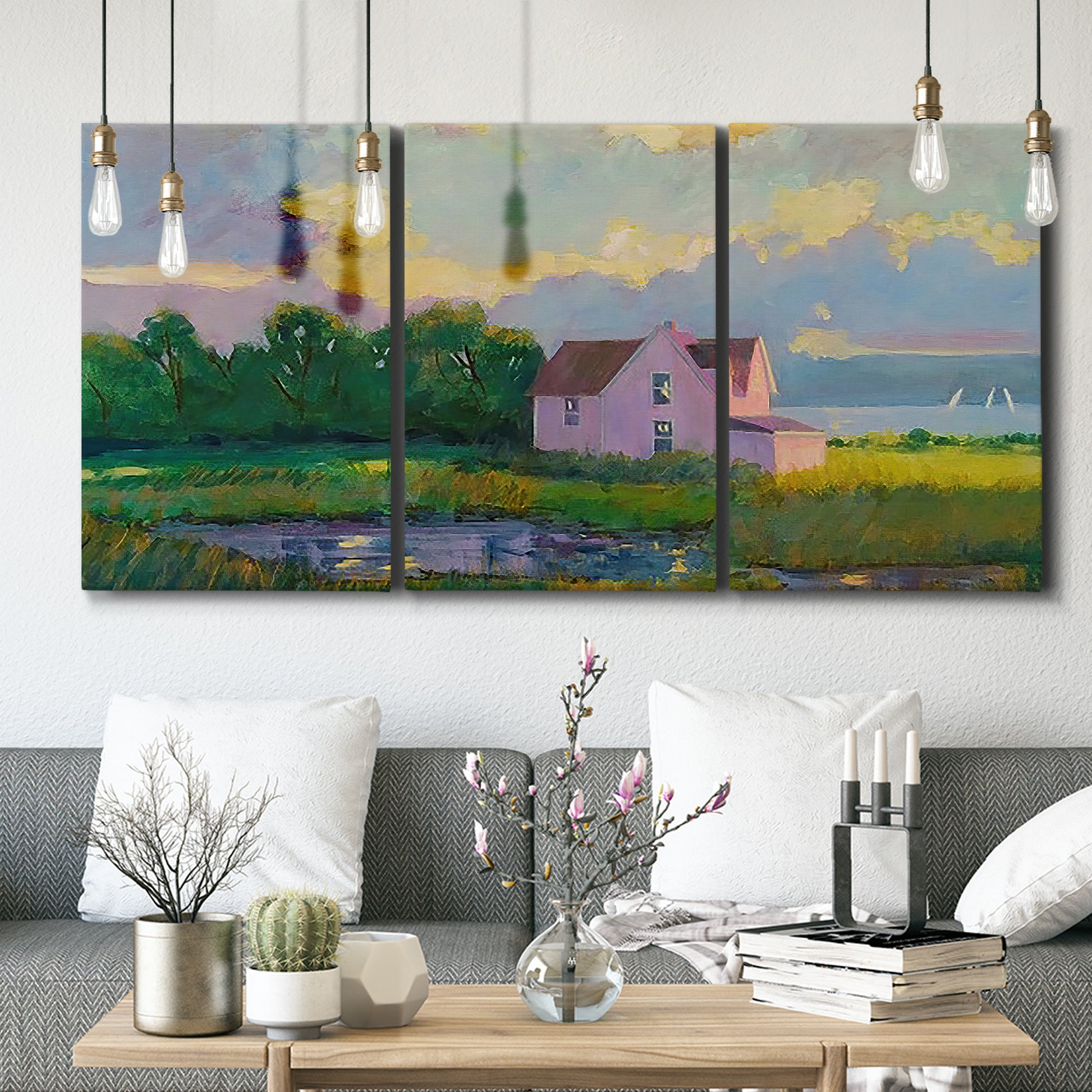 Three-panel canvas wall art featuring farmhouse near coastline landscape, displayed in a modern living room above seating.