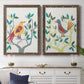 Set of two walnut barnwood framed canvas prints depicting a coordinated art pair of stylized colorful birds perched among leafy branches rendered as modern folk-art bird illustrations above a dining room sideboard.