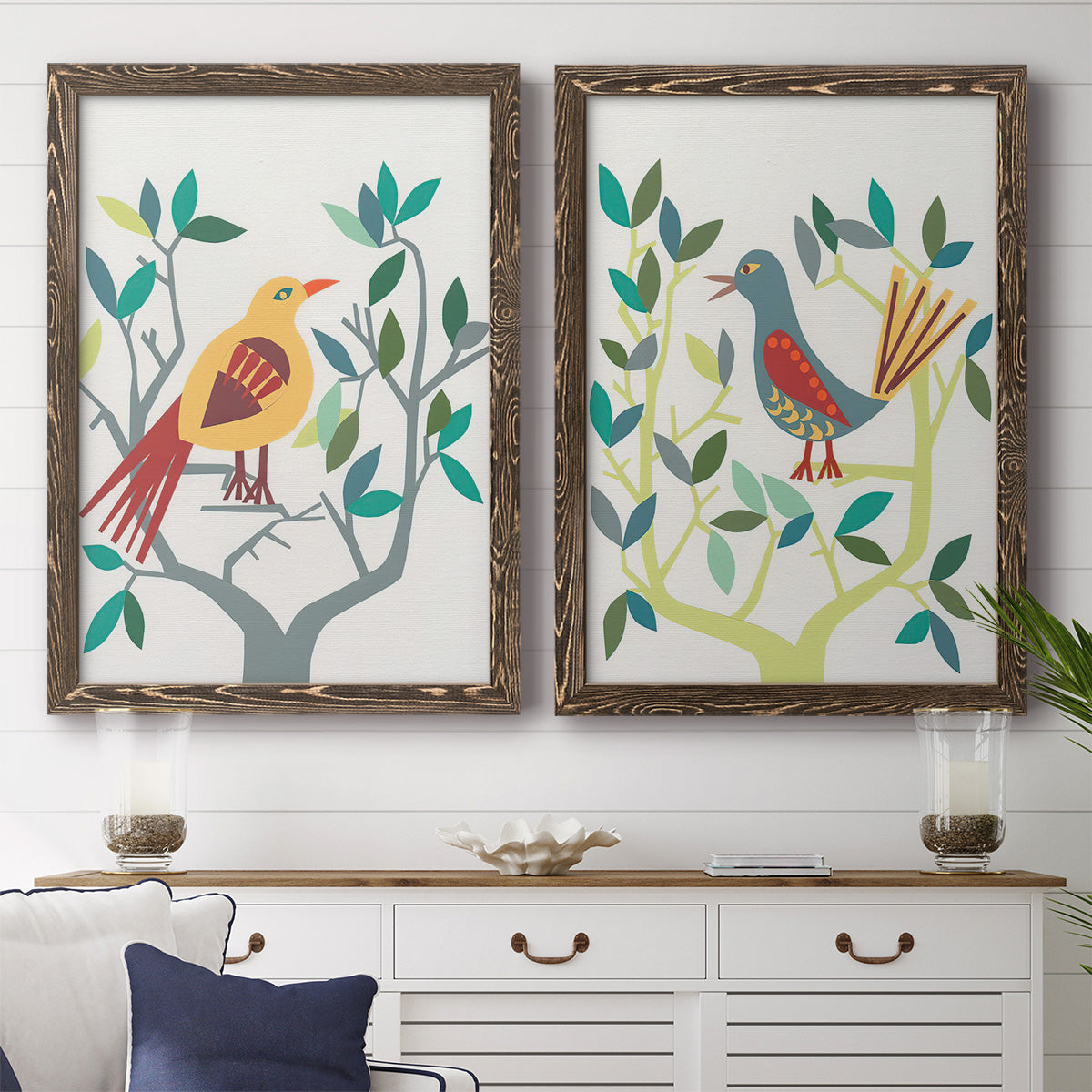 Set of two walnut barnwood framed canvas prints depicting a coordinated art pair of stylized colorful birds perched among leafy branches rendered as modern folk-art bird illustrations above a dining room sideboard.