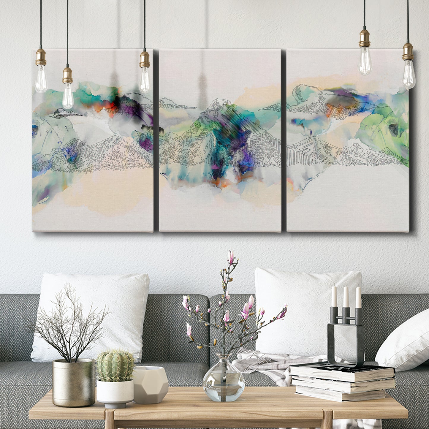 Three-panel canvas wall art featuring abstract mountain range watercolor, displayed in a modern living room above seating.