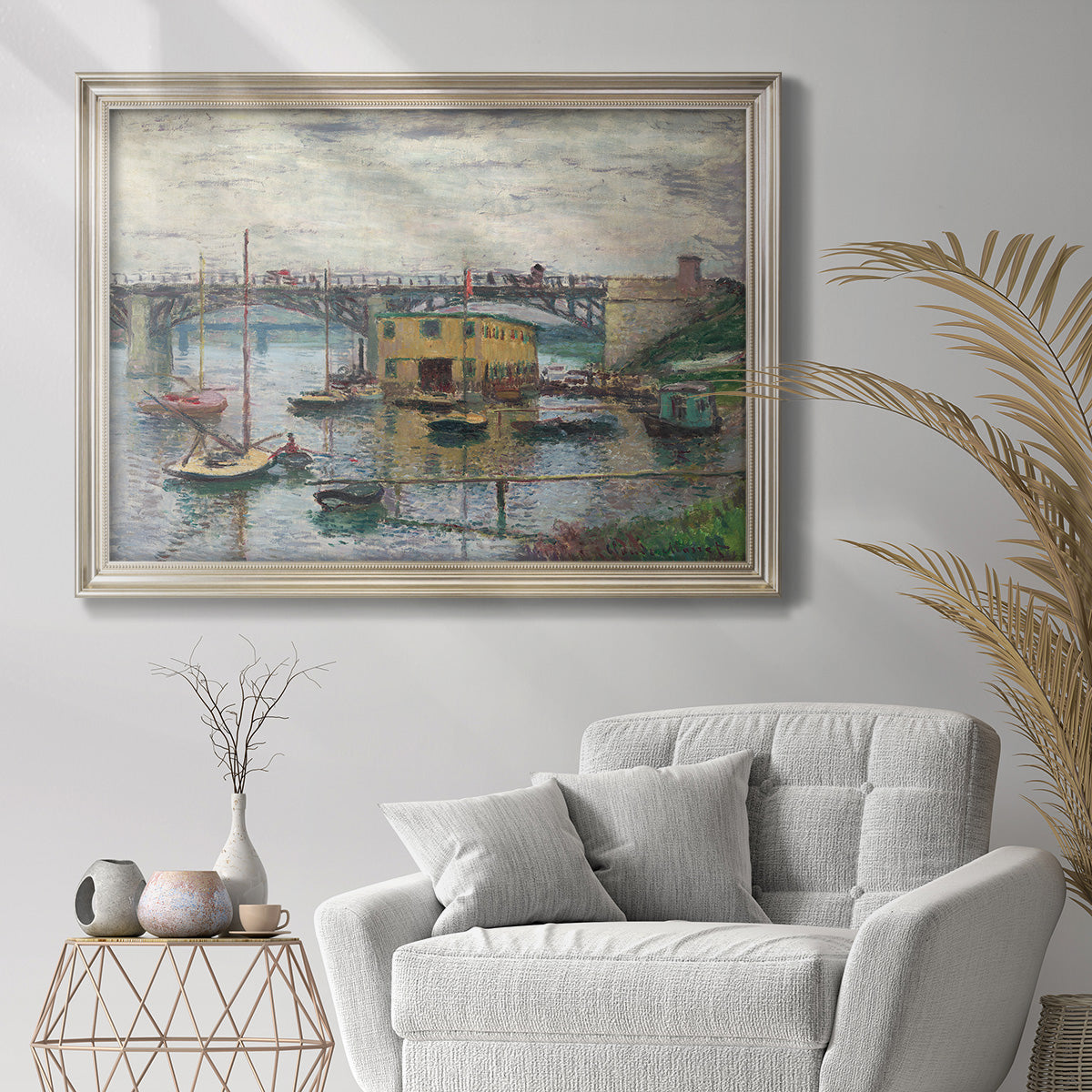 Impressionist river bridge scene on an overcast day by Claude Monet in an ornate champagne frame displayed in a bright interior setting.