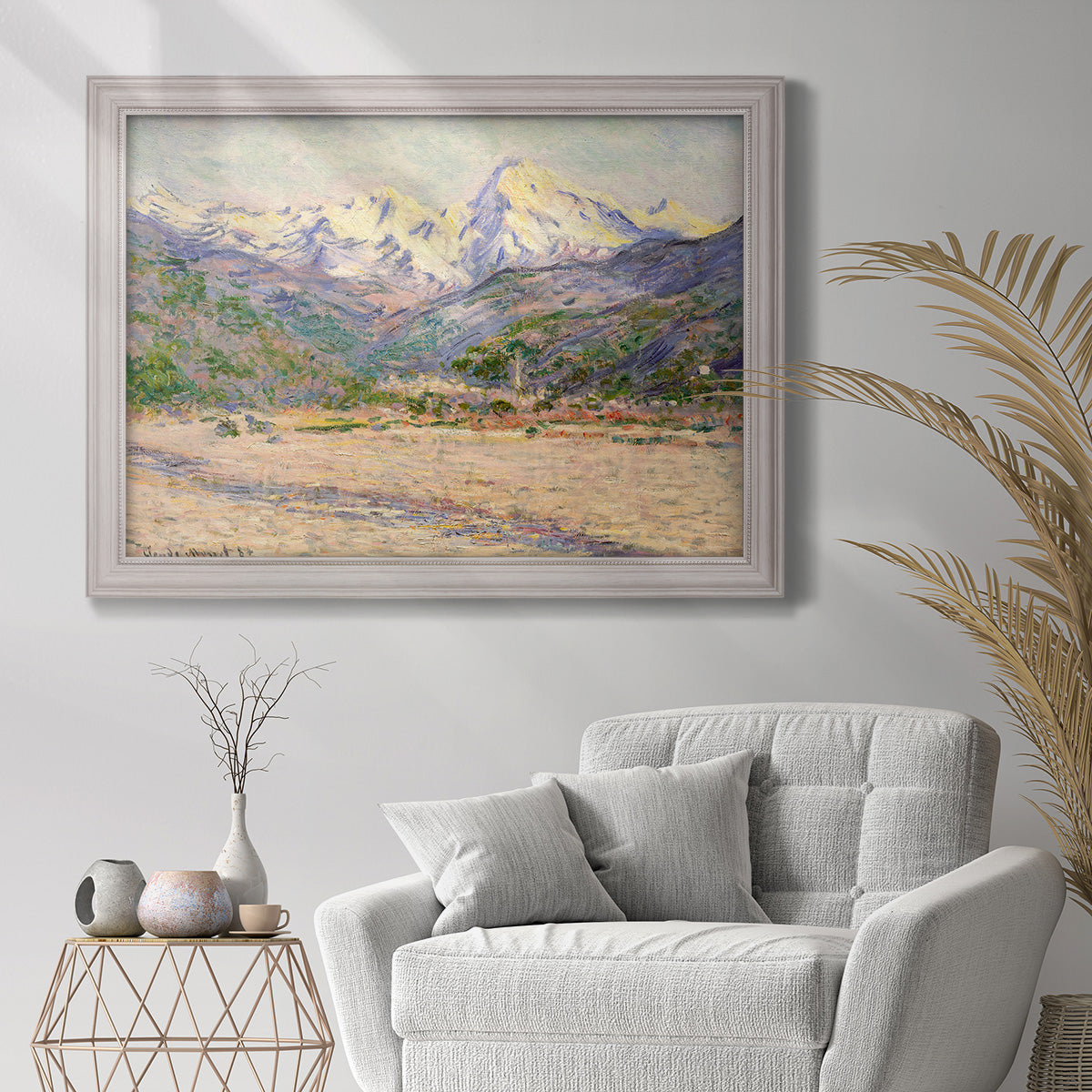 Impressionist valley landscape in southern France by Claude Monet in an ornate weathered white frame displayed in a bright interior setting.