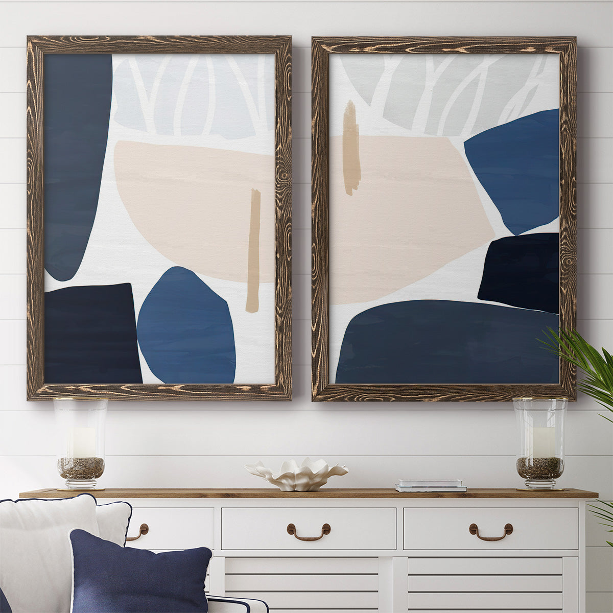 Set of two walnut barnwood framed canvas prints depicting a coordinated art pair of large navy cream and beige organic geometric shapes rendered as minimalist color-block abstracts above a dining room sideboard.