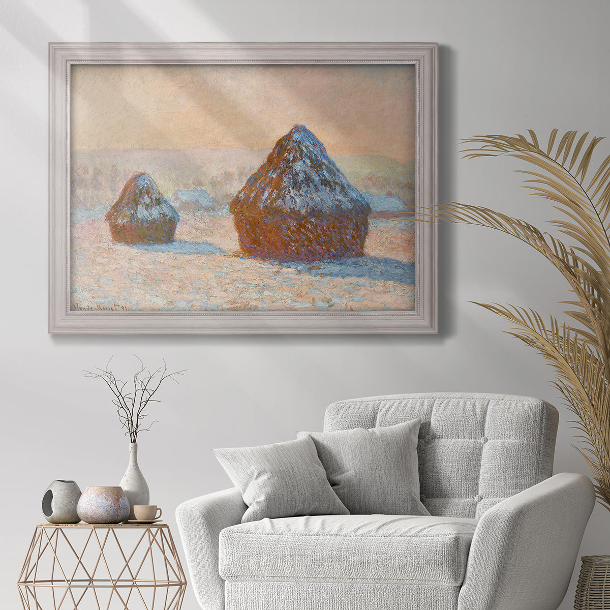 Impressionist winter haystack scene by Claude Monet in an ornate weathered white frame displayed in a bright interior setting.