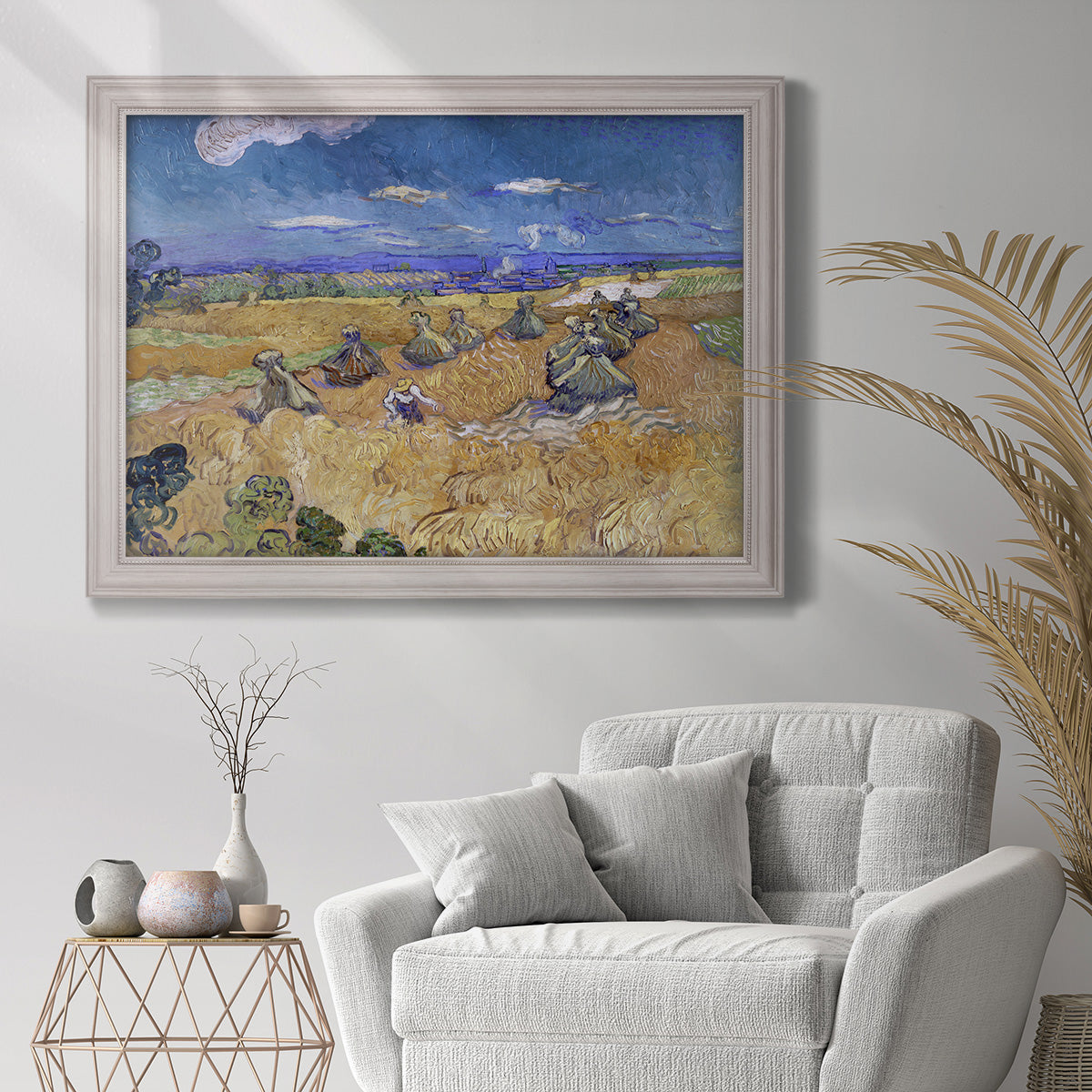 Impressionist wheat harvest scene by Vincent van Gogh in an ornate weathered white frame displayed in a bright interior setting.