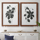 Set of two maple barnwood framed canvas prints depicting a coordinated art pair of black leafy vine silhouettes rendered as minimalist botanical prints above a dining room sideboard.