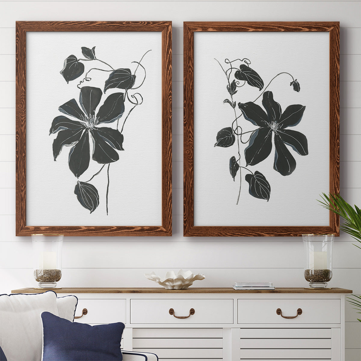 Set of two maple barnwood framed canvas prints depicting a coordinated art pair of black leafy vine silhouettes rendered as minimalist botanical prints above a dining room sideboard.