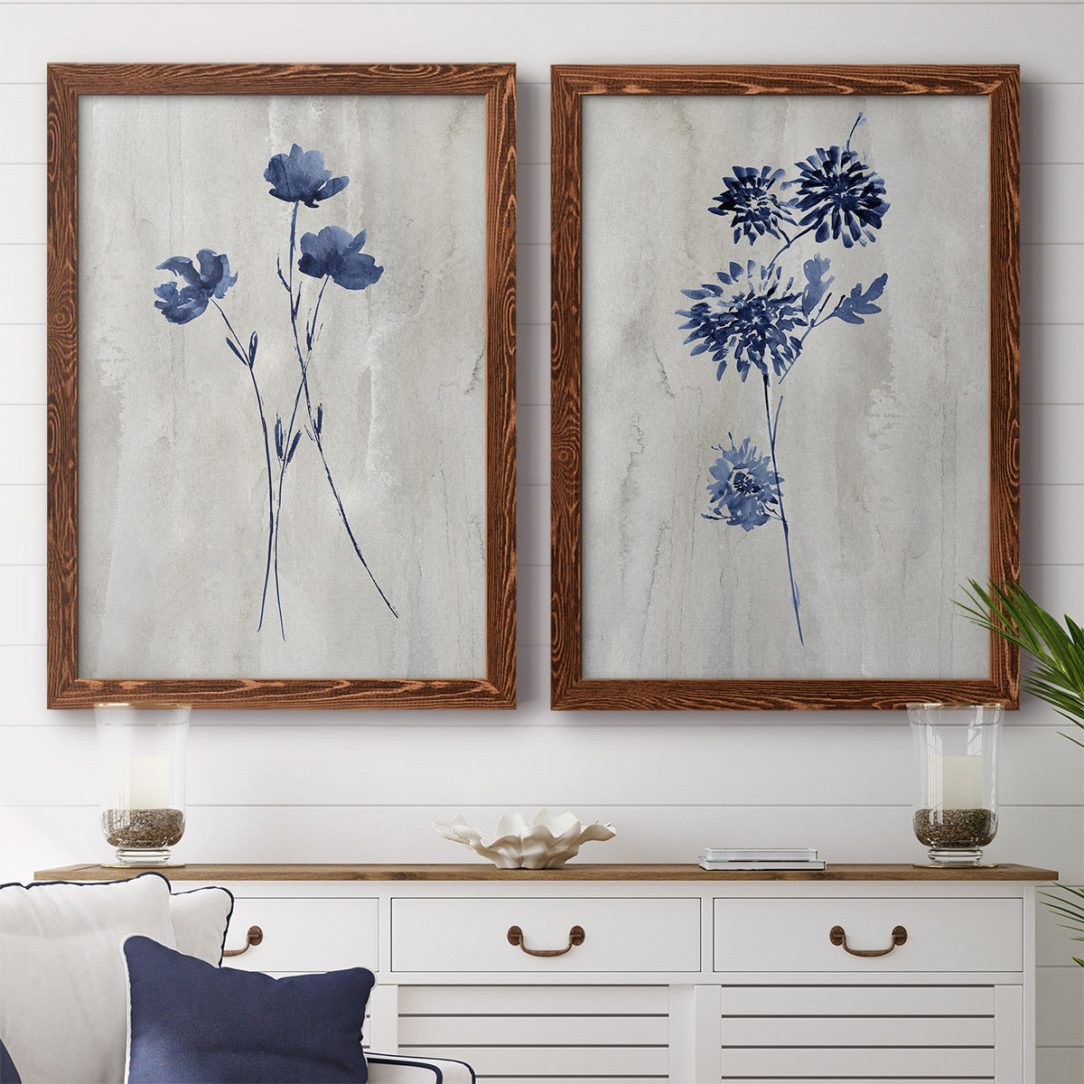 Set of two maple barnwood framed canvas prints depicting a coordinated art pair of blue wildflower stems on weathered neutral paper rendered as rustic monochrome botanical paintings above a dining room sideboard.