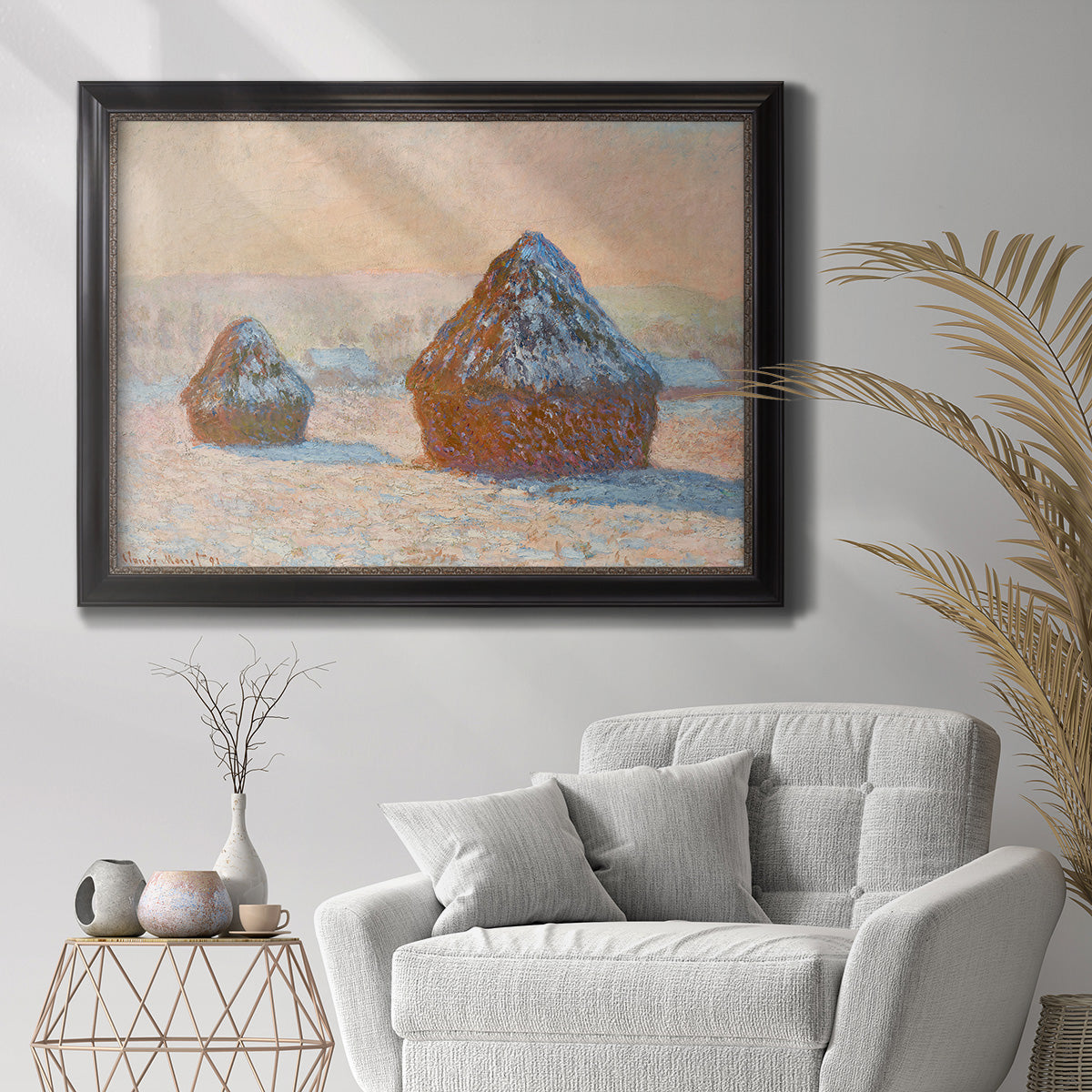 Impressionist winter haystack scene by Claude Monet in an ornate black frame with gilded inner detail displayed in a bright interior setting.