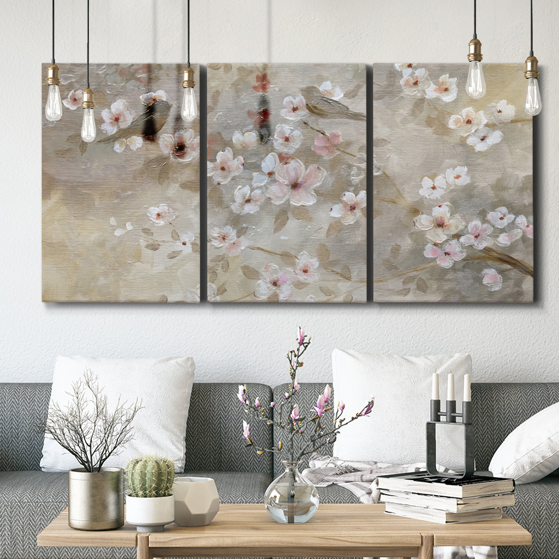 Three-panel canvas wall art featuring early spring blossoms in soft tones, displayed in a modern living room above seating.