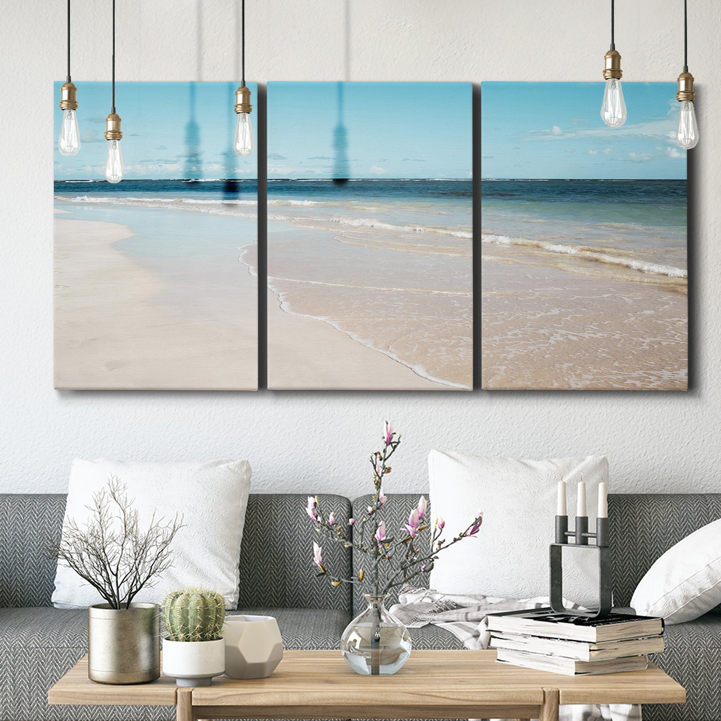Three-panel canvas wall art featuring white sand beach with gentle waves, displayed in a modern living room above seating.