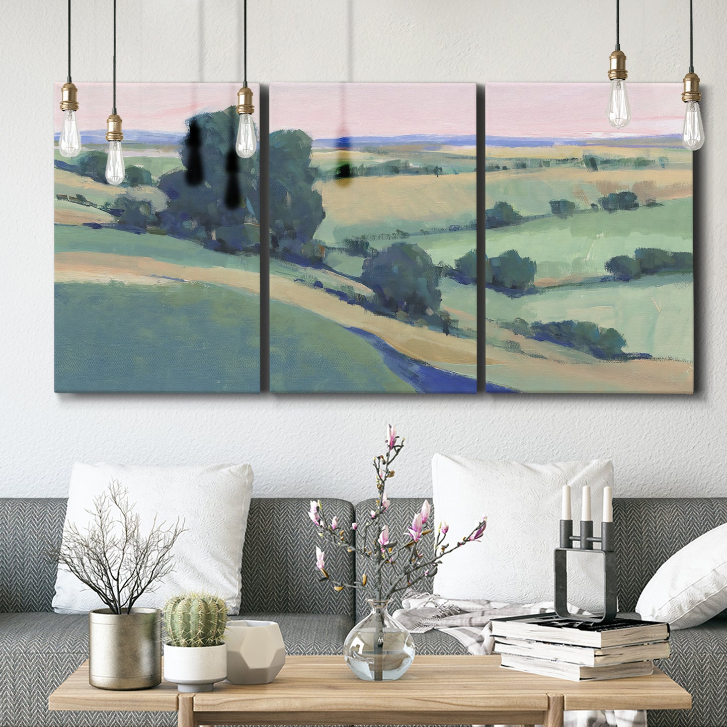 Three-panel canvas wall art featuring pastoral countryside with rocky outcrop, displayed in a modern living room above seating.