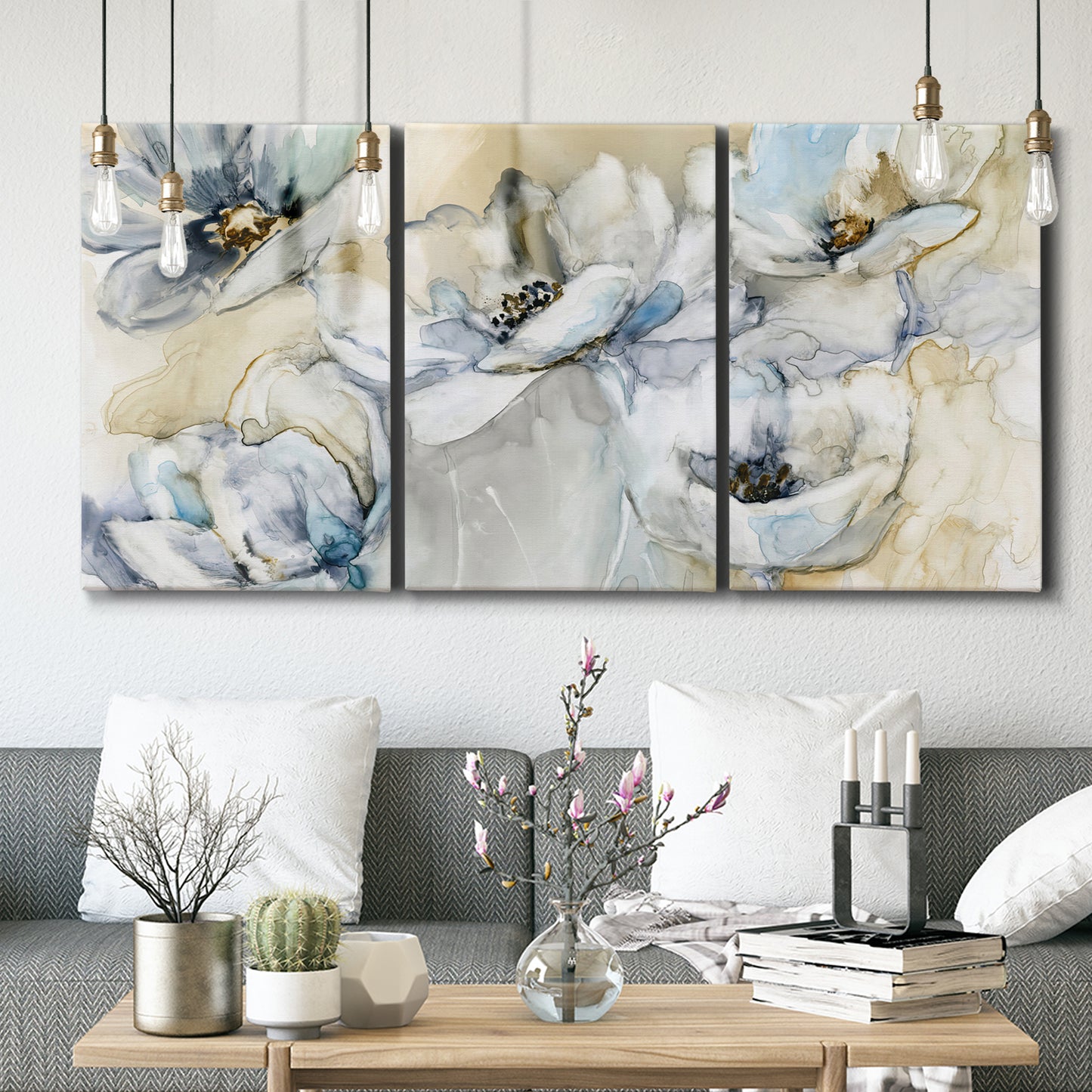 Three-panel canvas wall art featuring delicate watercolor floral blooms, displayed in a modern living room above seating.