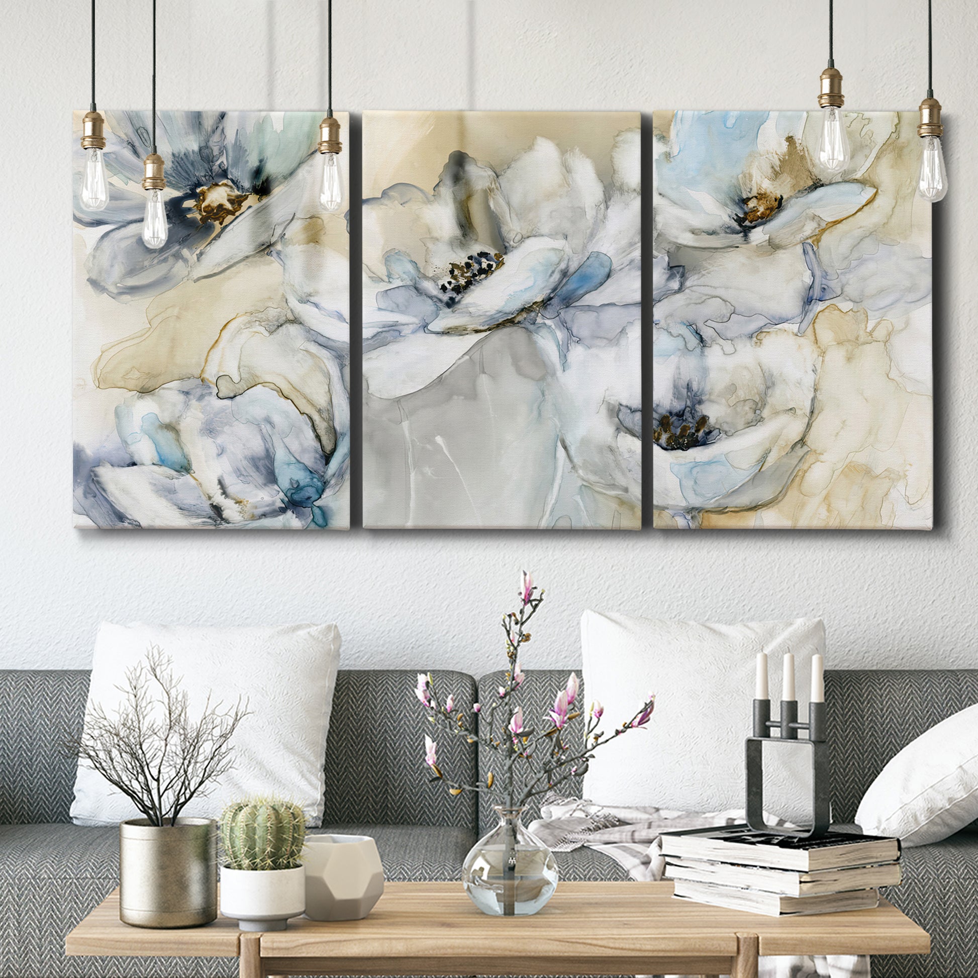 Three-panel canvas wall art featuring delicate watercolor floral blooms, displayed in a modern living room above seating.