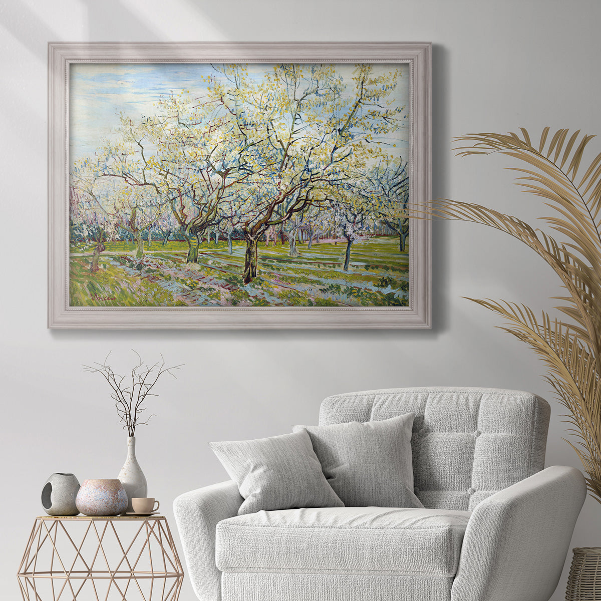 Impressionist white-blossomed orchard landscape by Vincent van Gogh in an ornate weathered white frame displayed in a bright interior setting.