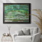 Impressionist garden scene with Japanese bridge and water lilies by Claude Monet in an ornate black frame with gilded inner detail displayed in a bright interior setting.