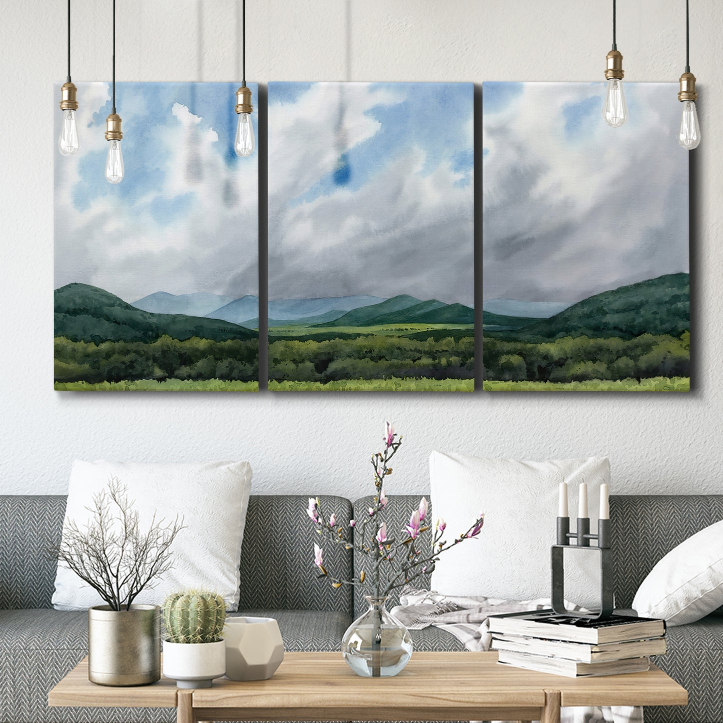 Three-panel canvas wall art featuring pastoral mountain landscape in blue, displayed in a modern living room above seating.