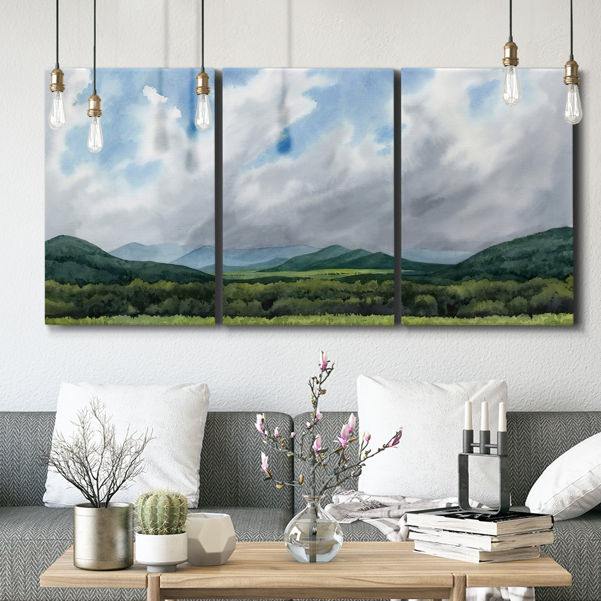Three-panel canvas wall art featuring pastoral mountain landscape in blue, displayed in a modern living room above seating.