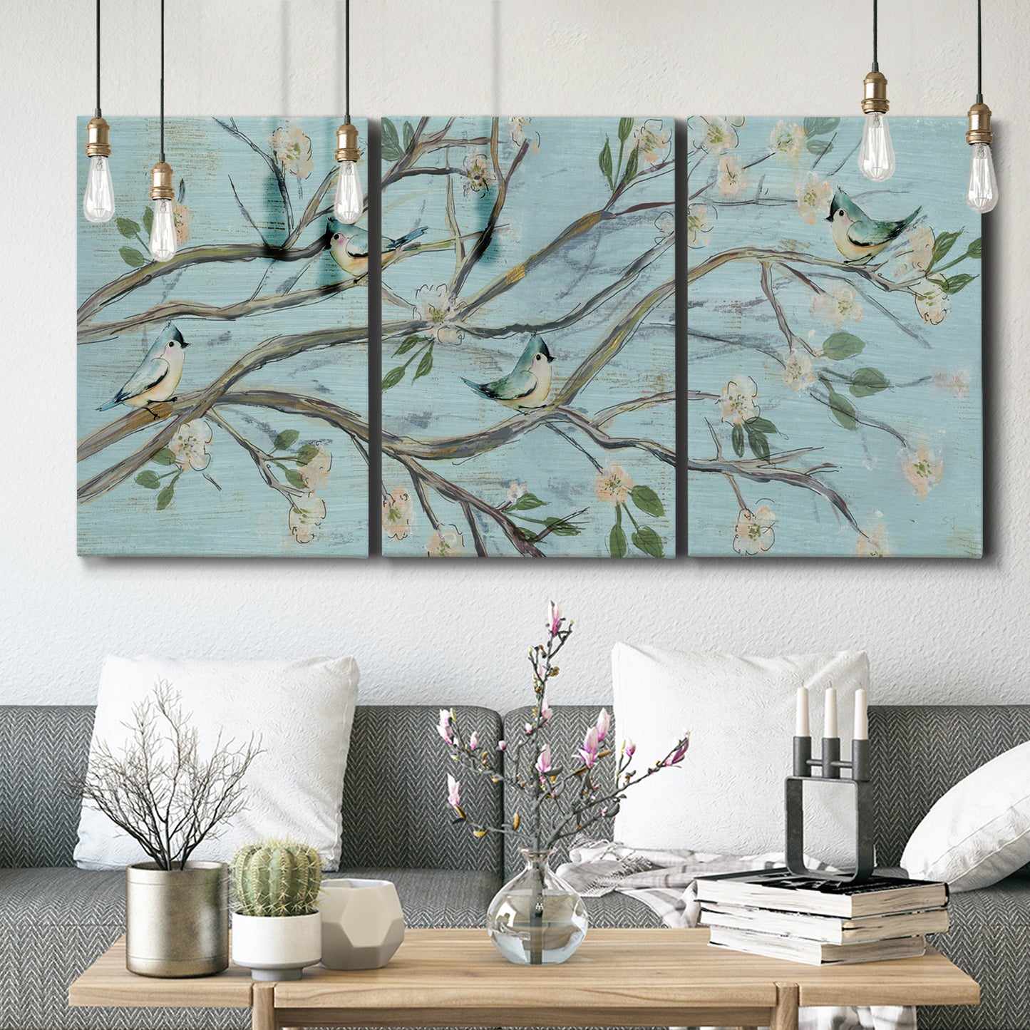 Three-panel canvas wall art featuring blue sky with flowering branches, displayed in a modern living room above seating.