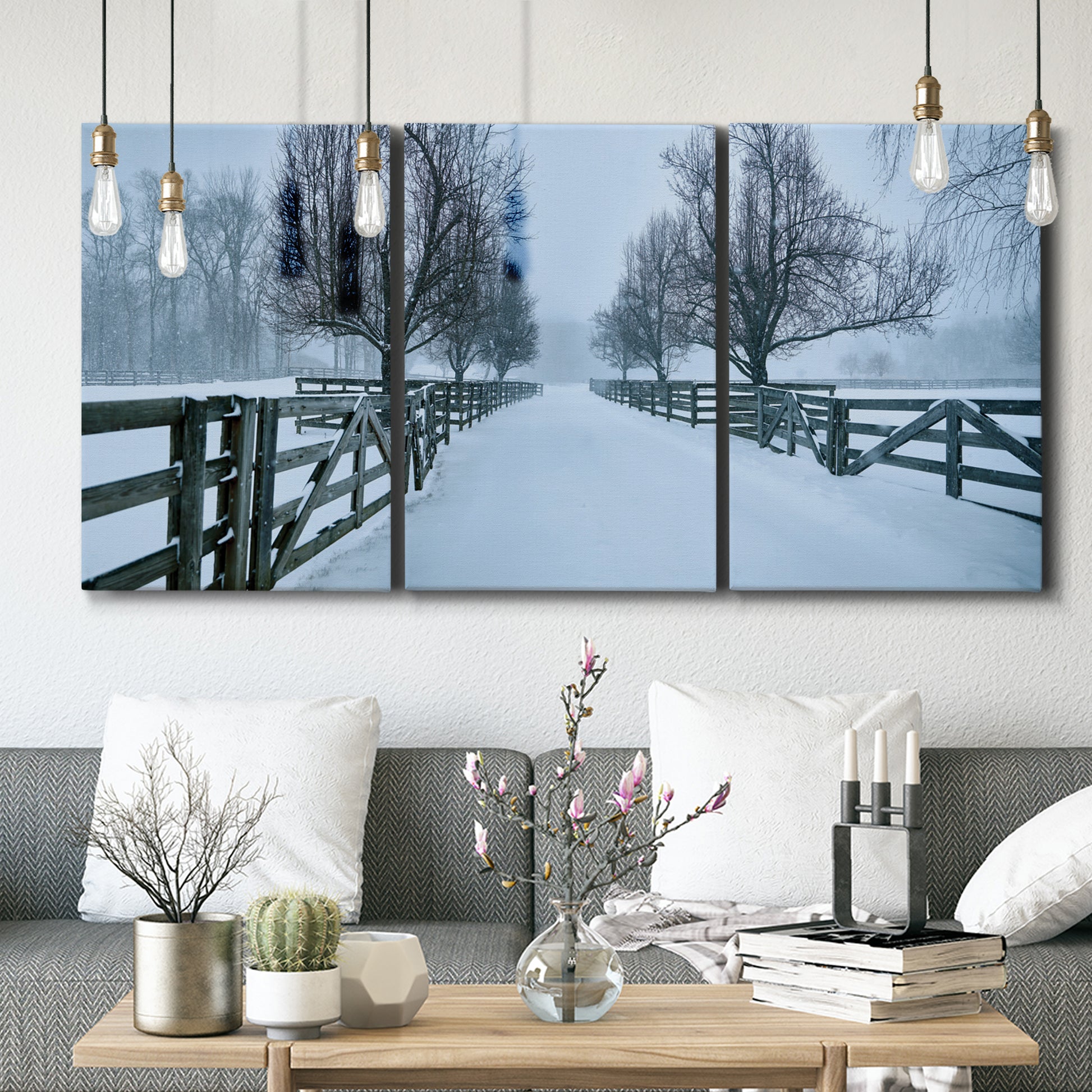 Three-panel canvas wall art featuring snow covered rural road photograph, displayed in a modern living room above seating.